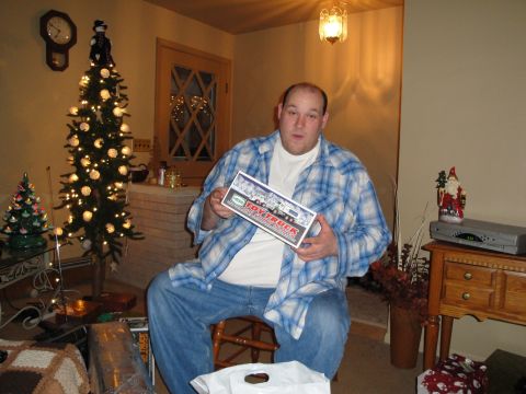 2000 Ford Crown Victoria - A man sits in a chair holding a toy truck box, surrounded by Christmas trees and decorations.