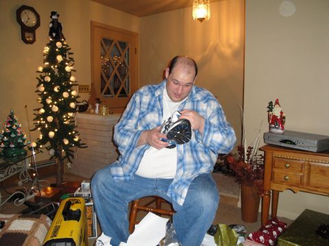 2000 Ford Crown Victoria - A man sits in a chair, opening a gift in a room decorated for Christmas, with a tree and presents visible.