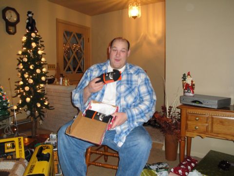 2000 Ford Crown Victoria - Man opening Christmas presents, including socks, with a decorated tree nearby.