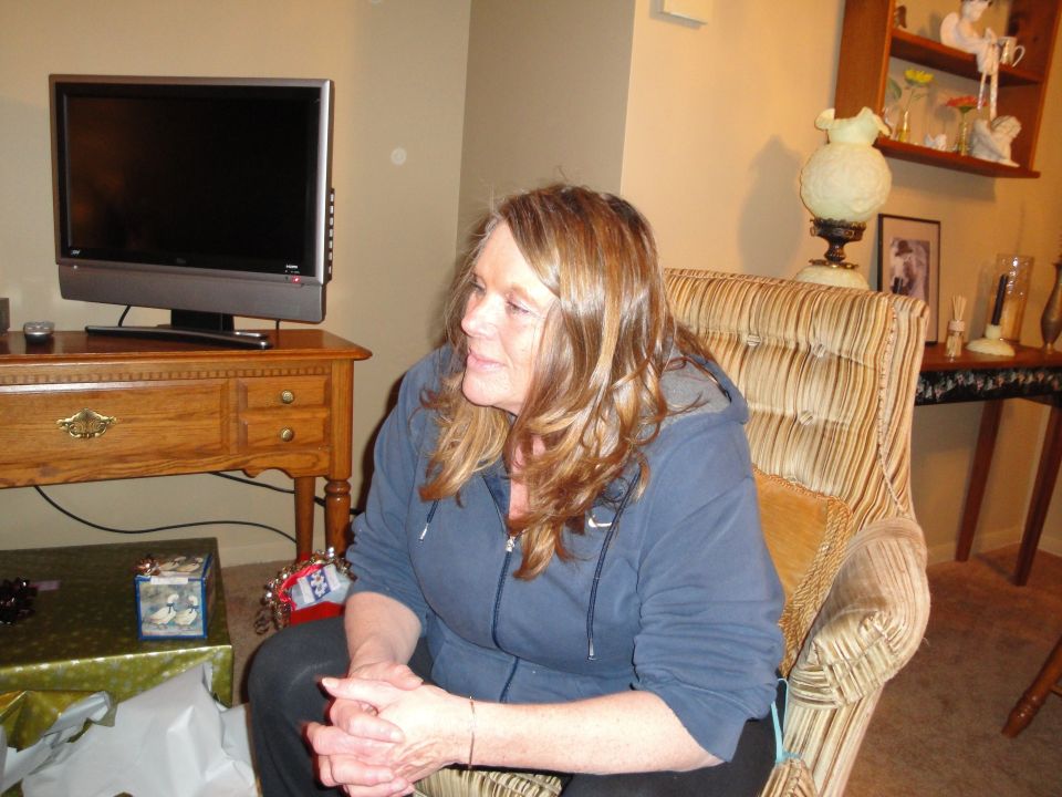Woman sitting in a striped armchair, looking to the side. A TV is on a wooden stand to her left