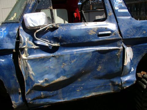 1979 Ford Bronco - The side of a heavily damaged blue pickup truck door is shown, covered in mud.