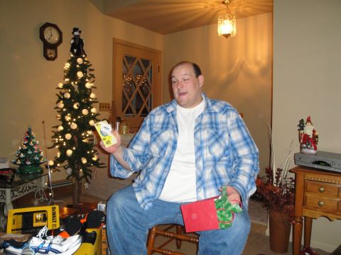 2000 Ford Crown Victoria - A man sits in front of a Christmas tree, holding gift tags and a red gift bag.