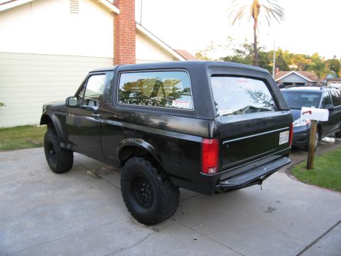 1986 Ford Bronco - This black Ford Bronco is parked in a driveway with a second vehicle visible behind it.