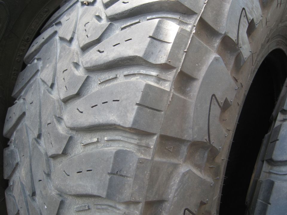 Close-up of a chunky off-road tire tread pattern. Some dashed lines are visible in the grooves