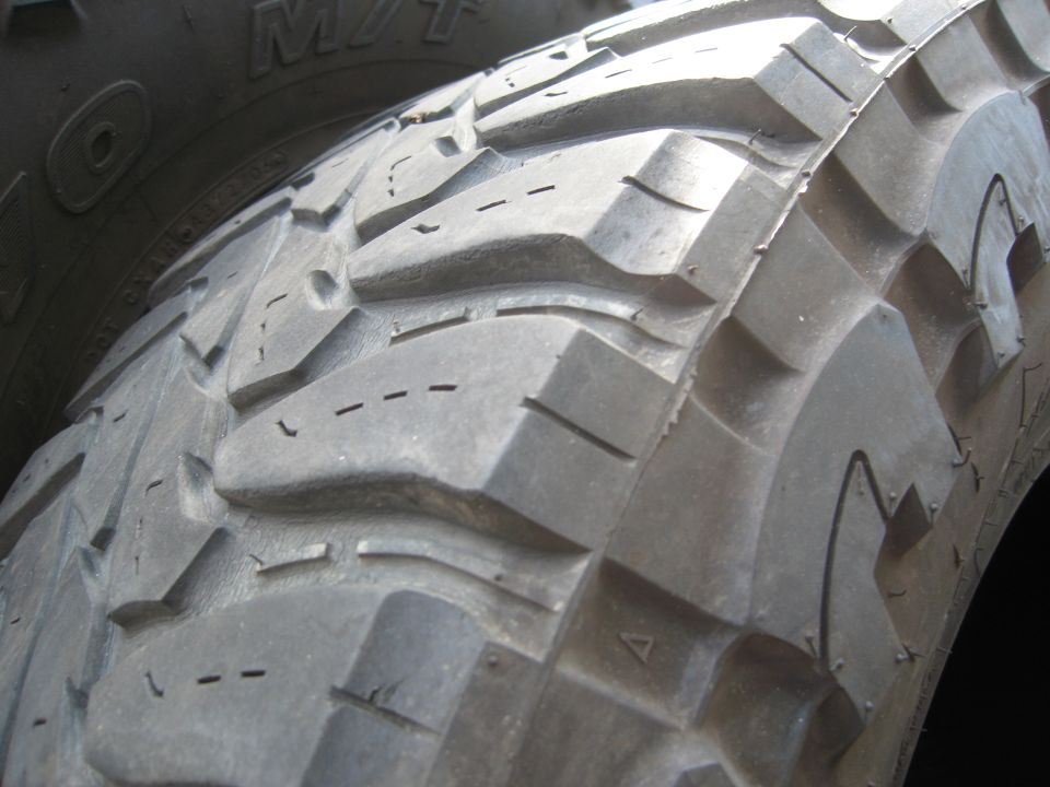 Close-up of a knobby off-road tire tread with visible "M/T" lettering on another tire in the background
