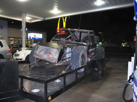 1986 Ford Bronco - Custom off-road buggy loaded onto a trailer at a gas station at night.