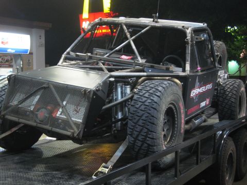 1986 Ford Bronco - Custom off-road race truck with roll cage and large tires is loaded onto a trailer.