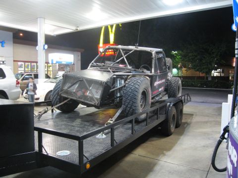 1986 Ford Bronco - A custom off-road buggy is loaded onto a trailer at a gas station at night.