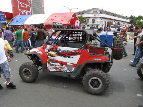 1986 Ford Bronco - A customized off-road UTV with racing decals is parked on a street with spectators around.