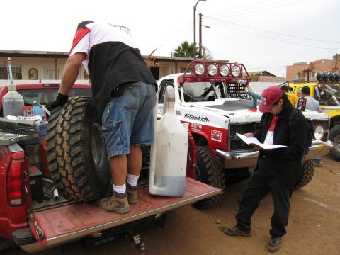 1986 Ford Bronco - Race trucks are being prepped with spare tires and fluids before an event.