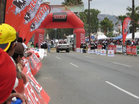 1986 Ford Bronco - Race vehicle crosses the finish line under a Tecate arch during an event.