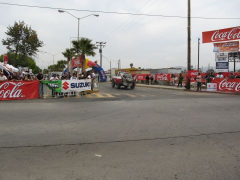 1986 Ford Bronco - A race truck passes under an inflatable archway during an event with Coca-Cola and Suzuki banners.