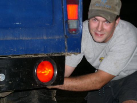 1979 Ford Bronco - A man is seen working on the rear of a blue truck, focusing on the taillight assembly.