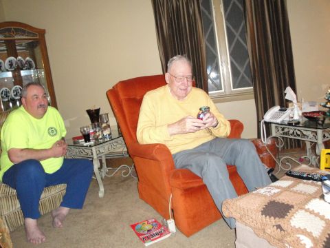 2000 Ford Crown Victoria - Two men are in a living room, one holding a small jar and the other sitting on a couch.