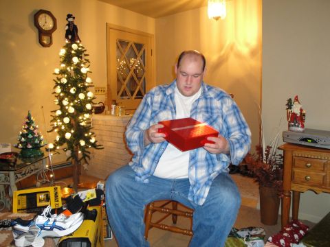2000 Ford Crown Victoria - A man sits in a chair, holding a red gift box, with a decorated Christmas tree in the background.