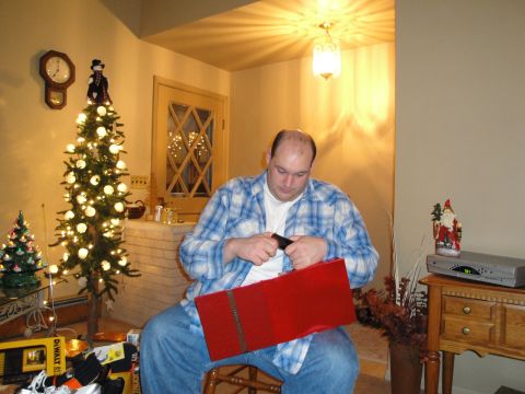 2000 Ford Crown Victoria - A man sits in a chair, focused on opening a large red gift box during the holiday season.