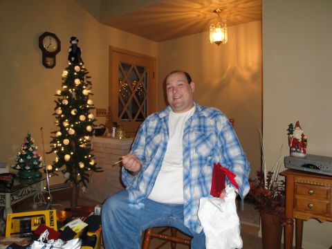 2000 Ford Crown Victoria - A man sits in a chair next to a decorated Christmas tree, holding a gift.
