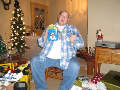 2000 Ford Crown Victoria - Man sits with Christmas gifts and a card, with a decorated tree in the background.