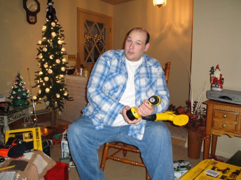 2000 Ford Crown Victoria - A man sits in a chair holding a yellow power tool, with a decorated Christmas tree and gifts visible in the room.
