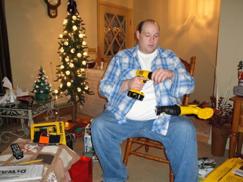 2000 Ford Crown Victoria - A man sits in a chair, assembling a yellow DeWalt reciprocating saw while holding a yellow DeWalt drill, with a Christmas tree in the backg…