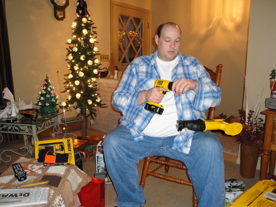 Man holding yellow DeWalt drill and reciprocating saw near Christmas tree