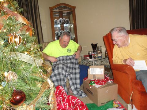 2000 Ford Crown Victoria - Two men exchange gifts on Christmas morning, with a decorated tree and presents scattered around the room.
