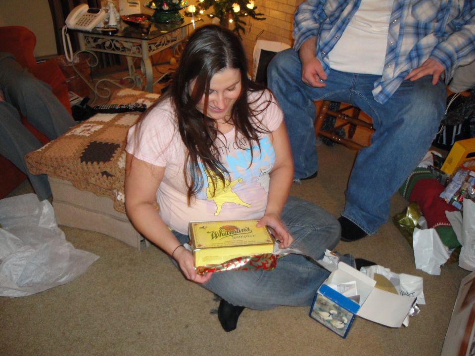 Woman opening a Whitman's chocolate box in a living room with Christmas decorations