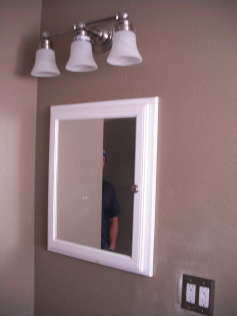 1991 Ford Bronco - A bathroom scene with a triple-bulb vanity light and a medicine cabinet reflecting a person.