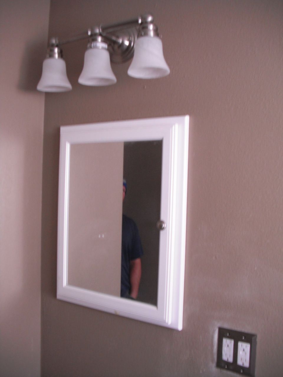 Bathroom vanity light above a white medicine cabinet with a reflection of a person