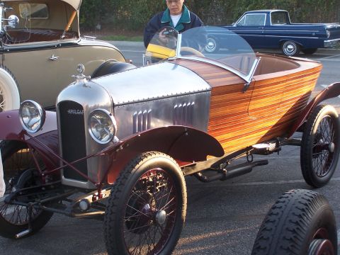 1990 Ford Bronco - A vintage Amilcar car with a wooden body is parked next to another car, with a person standing behind it.