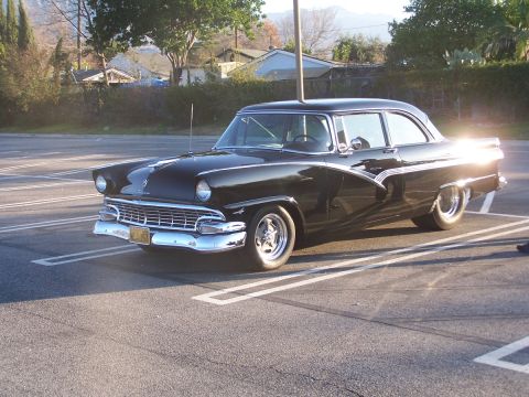 1990 Ford Bronco - A black 1956 Ford Fairlane sedan is parked in a lot, showing its classic body style.