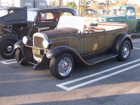 1990 Ford Bronco - A weathered convertible hot rod is parked next to other vehicles, displaying a California license plate.