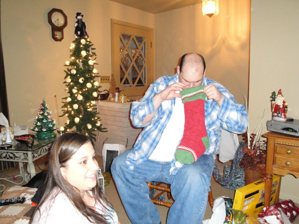 Christmas tree with lights and ornaments, a man holding a stocking, and a woman in a living room