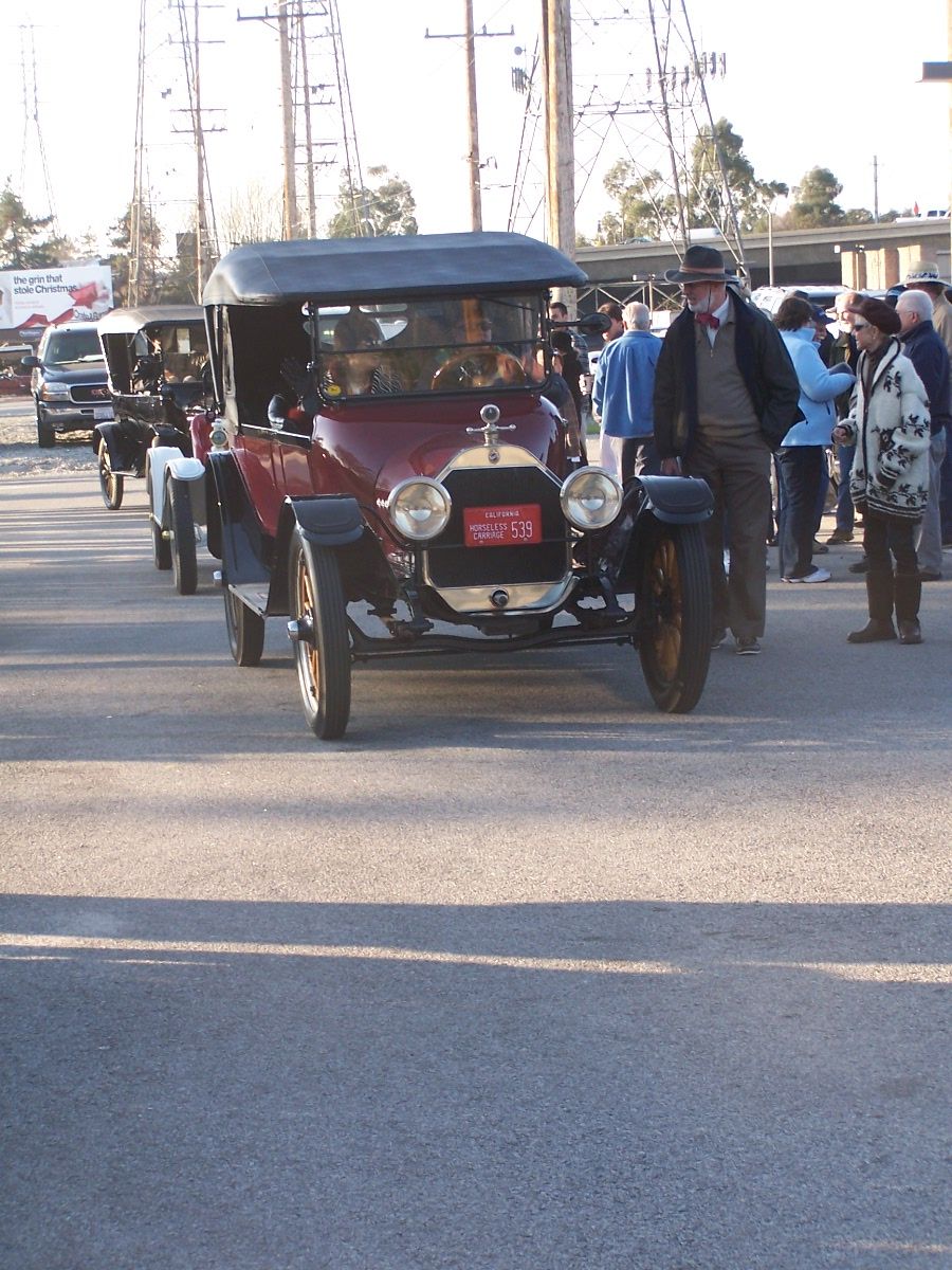 Line of old cars, one is a red touring car with a black top and a man in a hat standing next to it