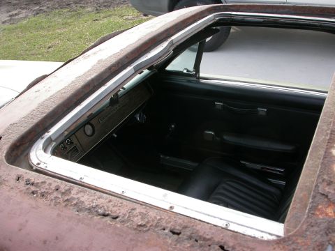 1968 Mercury Cougar - The interior of a 1968 Mercury Cougar is visible through the open sunroof, showing black seats and a woodgrain dashboard.