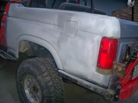 1985 Ford Bronco - Ford Bronco undergoing bodywork, showing primer on the rear quarter panel and a large off-road tire.