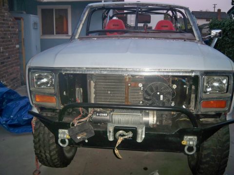 1985 Ford Bronco - This white SUV, likely from the early 1980s, features an aftermarket bumper and winch, with red racing seats visible inside.