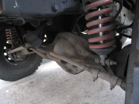 1986 Ford Bronco - The underside of a vehicle shows the front axle, steering components, and suspension system with red springs.