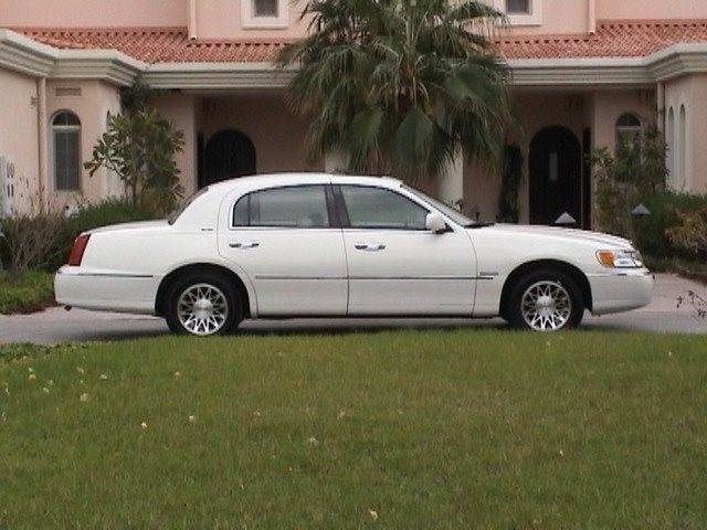 White Lincoln Town Car sedan in side profile on a driveway by a pink stucco house