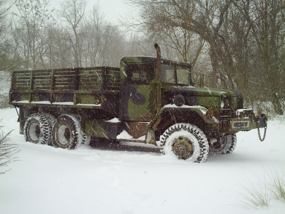 Military truck with camouflage paint stuck in snow, trees in background