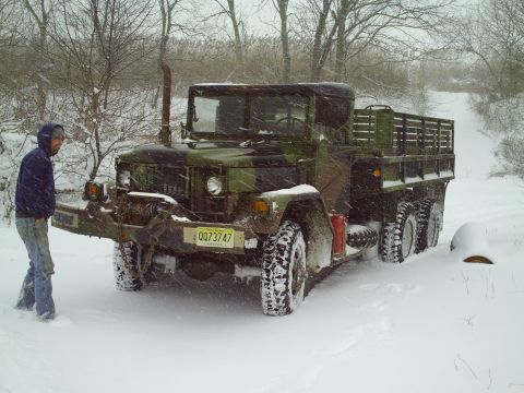 1990 Ford Bronco - A man stands by a camouflage military truck stuck in the snow during a winter storm.