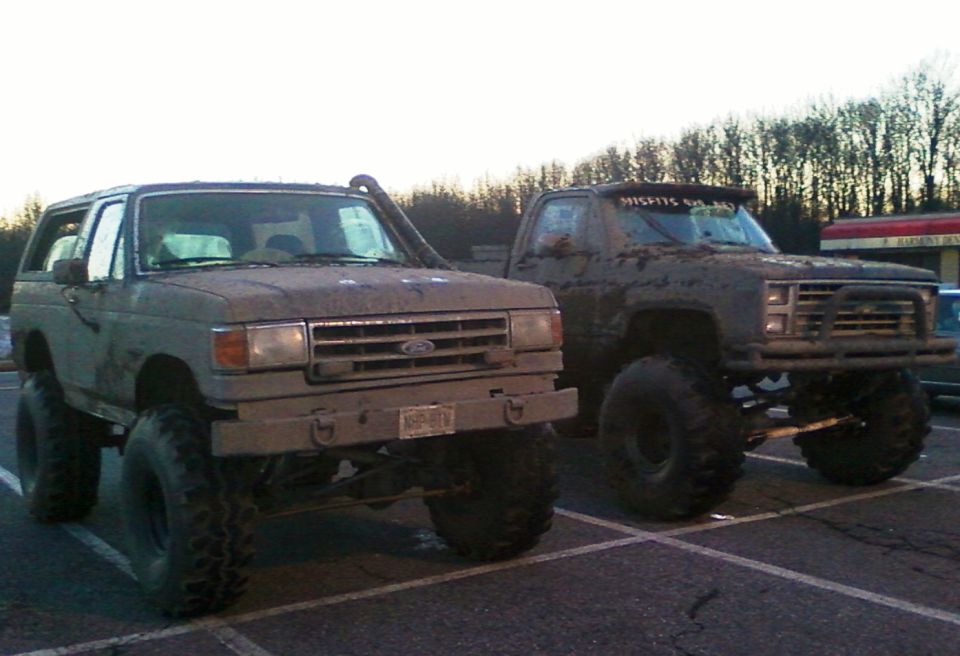 1990 Ford Bronco and lifted pickup truck covered in mud