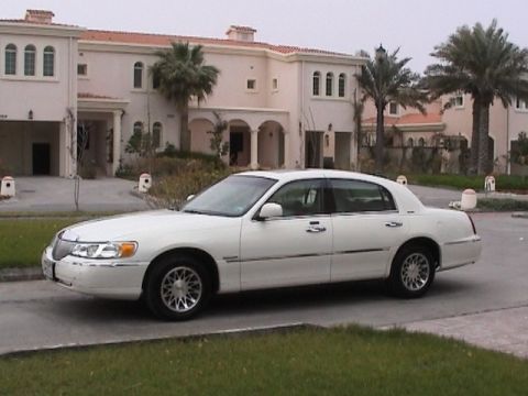 2002 Lincoln Town Car - This white 2002 Lincoln Town Car is parked on the street in front of a large house.