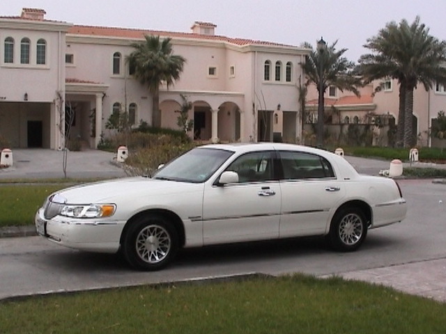 White Lincoln Town Car sedan on chrome spoke wheels parked outside stucco villas with palms