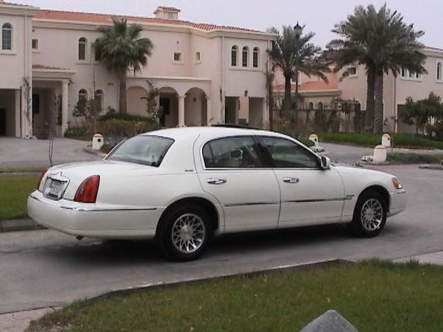 White Lincoln Town Car sedan, rear three-quarter view, parked by tan villas