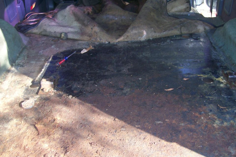 Interior of a vehicle showing torn upholstery and a rusty, damaged floor