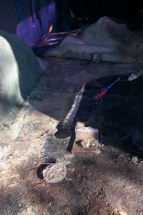 1992 Ford C-350 (Centurion Conversions) - The floor of a vehicle's interior shows signs of rust and damage, with a screwdriver lying nearby.