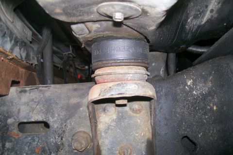 1992 Ford C-350 (Centurion Conversions) - Close-up of a body lift spacer on a heavily rusted vehicle frame and suspension components.