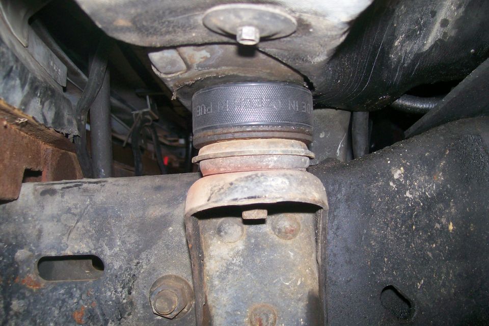 Body lift spacer installed between frame and suspension component on a rusty vehicle