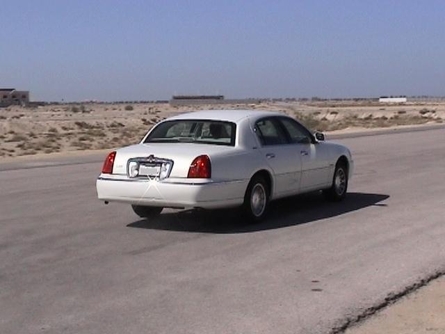 White Lincoln Town Car sedan, 3q rear, on a desert road under blue sky